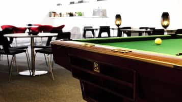 A pool table with a green felt surface and a yellow cue ball, surrounded by black chairs and a red chair.