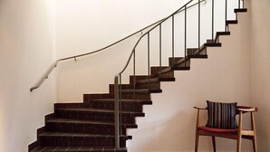 Una escalera con escalones de ladrillo oscuro y barandales de metal, que conduce a una plataforma. Una silla de madera con cojín a rayas está colocada en la plataforma.