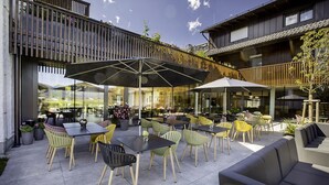 An outdoor seating area with tables and chairs, a covered section, and a view of the interior through large windows.