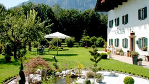 A hotel with a garden, outdoor seating, and a mountain backdrop.