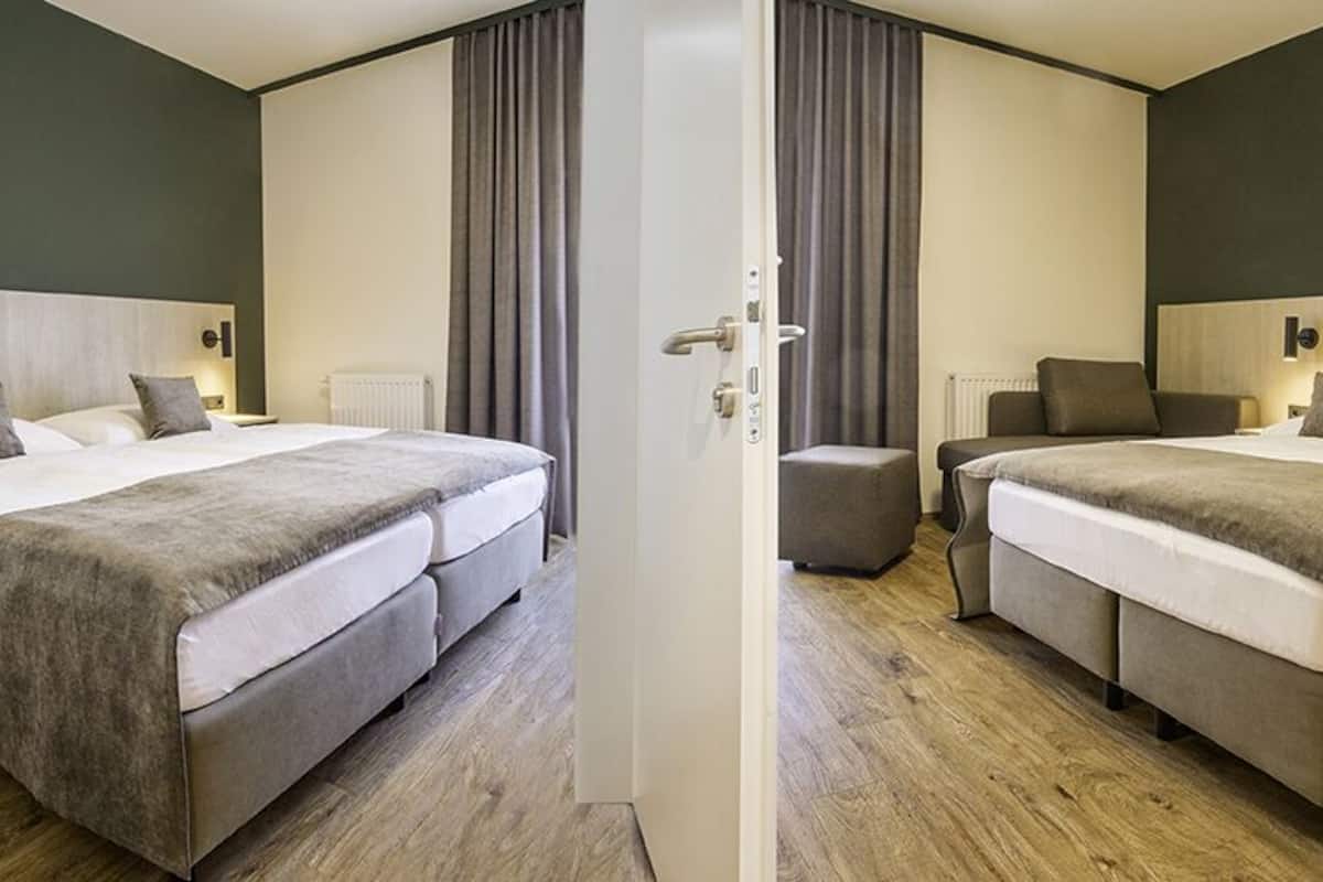 A modern hotel room with two beds, a sofa, a small table, and a door.