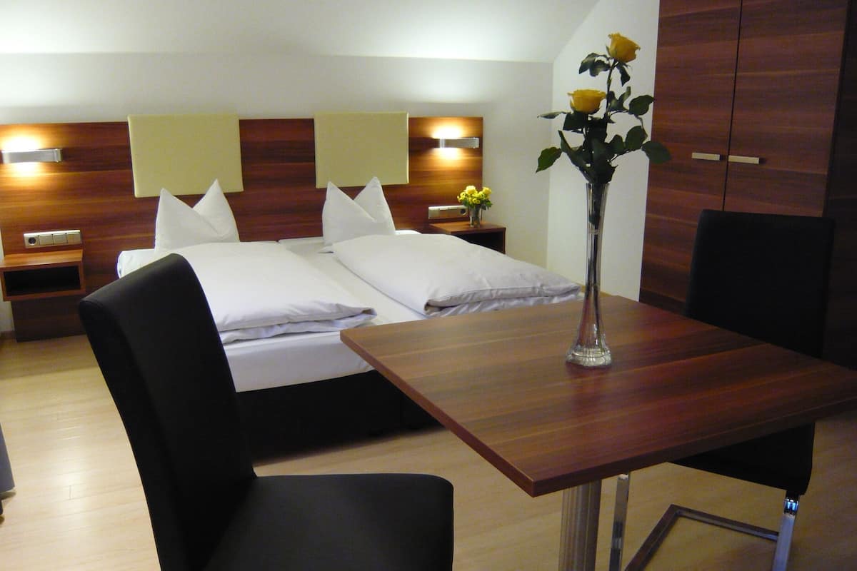 A hotel room with a bed, a desk, a chair, a nightstand, and a vase with flowers.