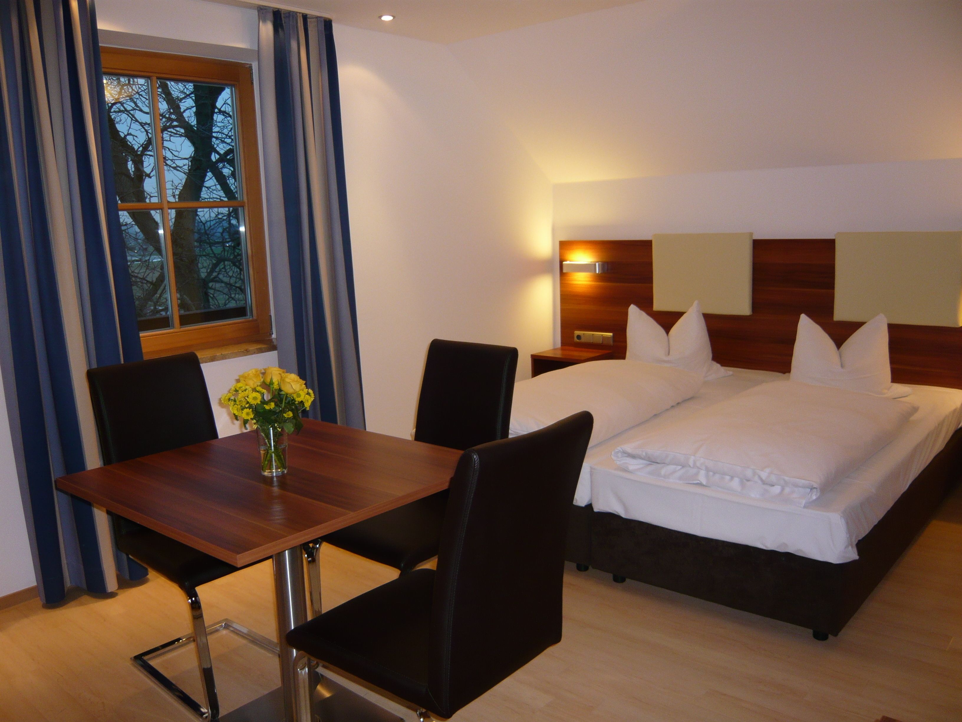 Ein Hotelzimmer mit einem hölzernen Bett, einem Nachttisch, einem Schreibtisch mit Stühlen und einem Fenster mit Vorhängen.