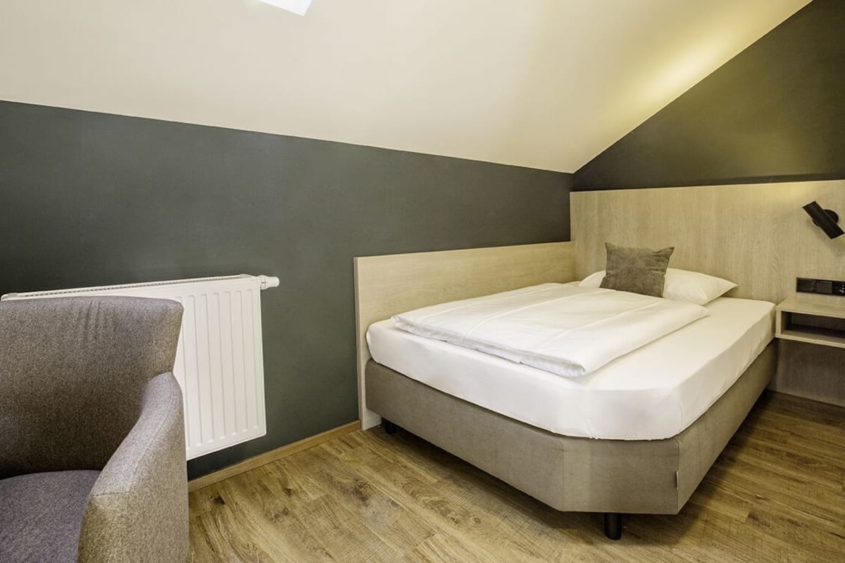 A modern bedroom with a bed, a chair, a bedside table, and a radiator.
