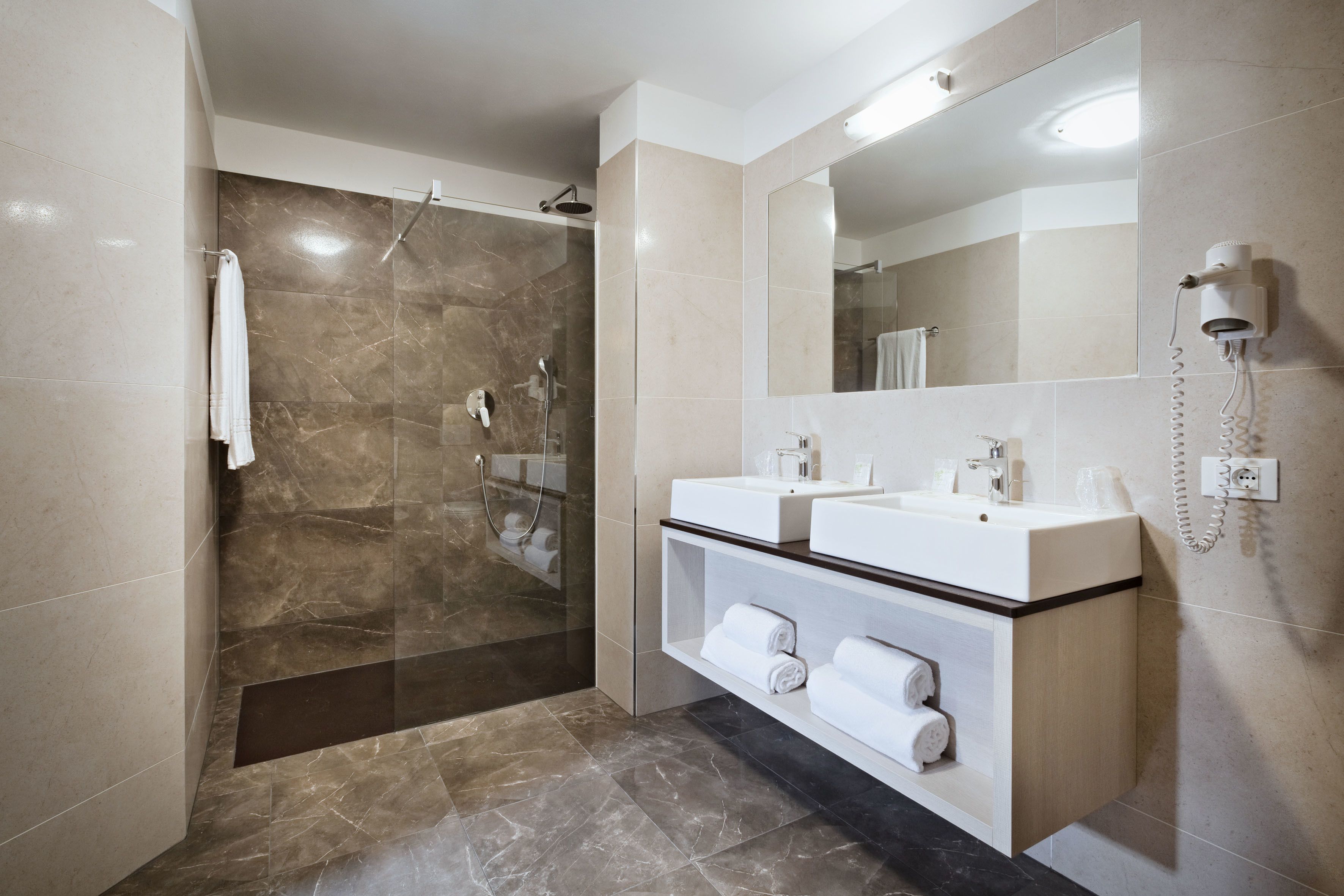 A modern bathroom with a glass-enclosed shower, a vanity with two sinks, and a built-in hairdryer.