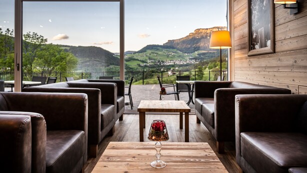 A restaurant with leather seating, a wooden table with a glass, and a view of a valley.