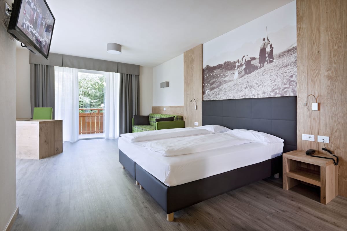 A modern hotel room with a large bed, a television, a balcony, and a wooden accent wall.