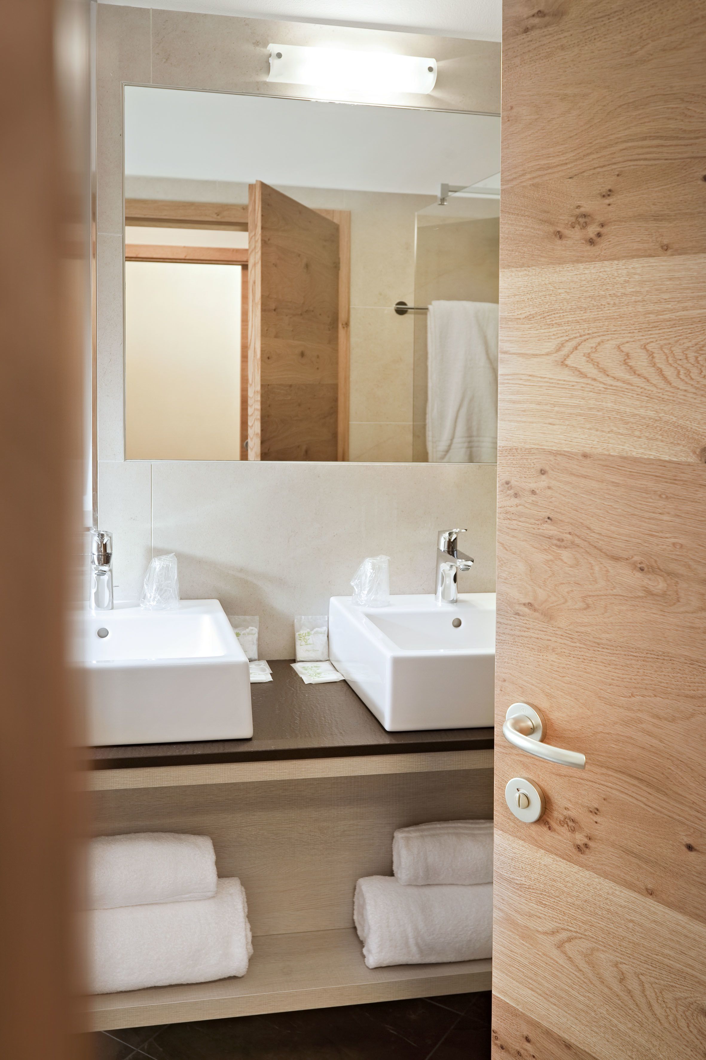 A modern bathroom with two sinks, a mirror, and wooden shelves with towels.