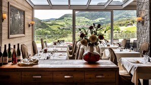 A dining area with a table set for a meal, a vase of flowers, and a scenic view of the countryside through large windows.