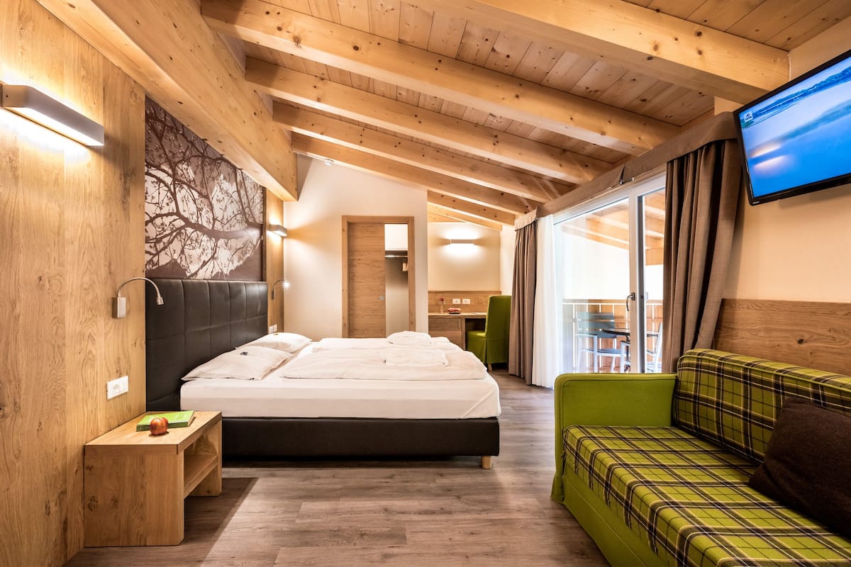 A modern hotel room with a wooden ceiling, a large bed, a green sofa, and a flat-screen TV.