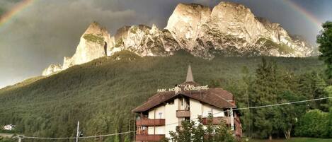 Un hotel con montañas al fondo y un arcoíris.