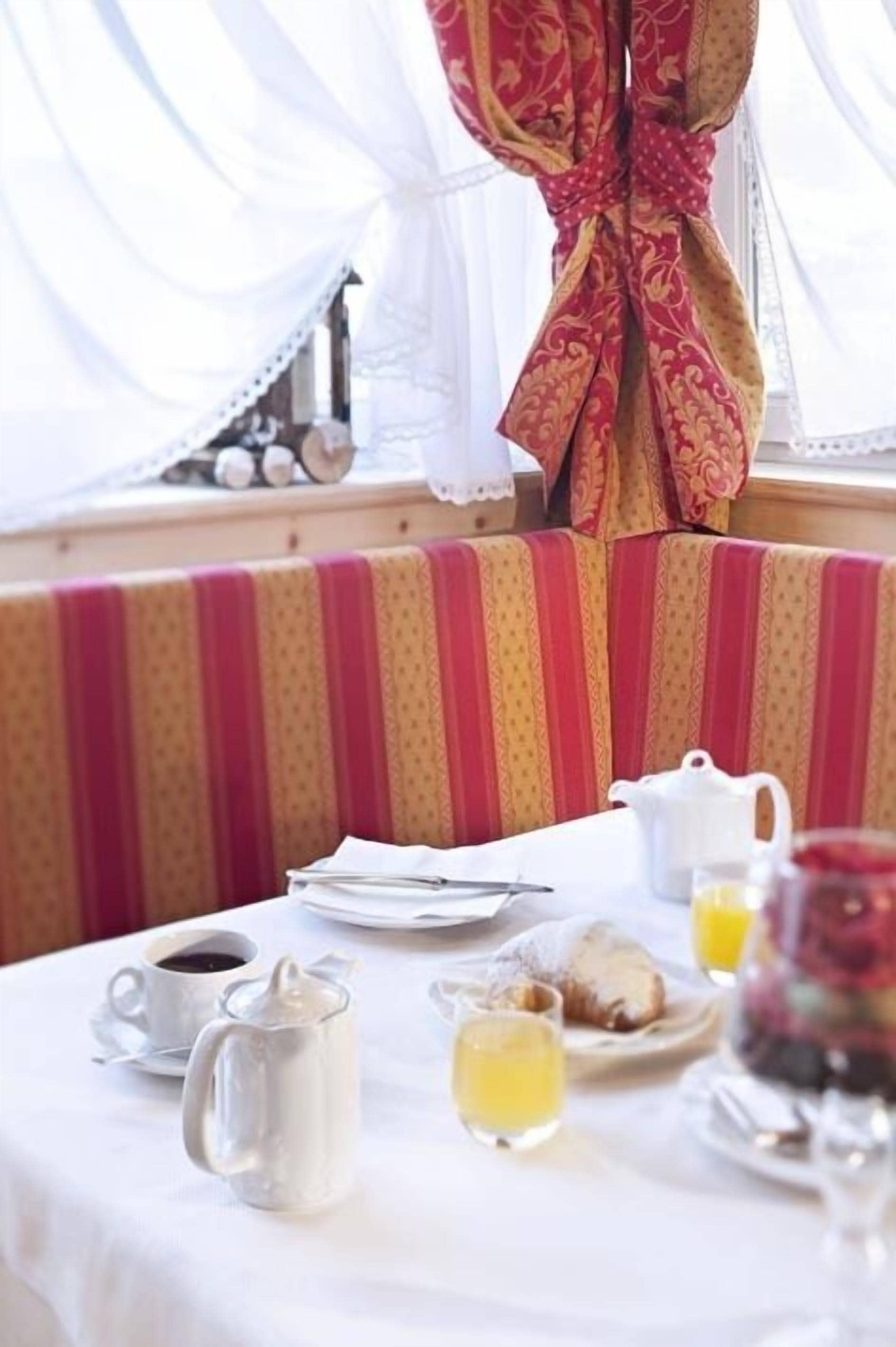 Une table de petit-déjeuner dressée avec une cafetière, des tasses, une théière, une assiette de viennoiseries et un verre de jus d’orange.