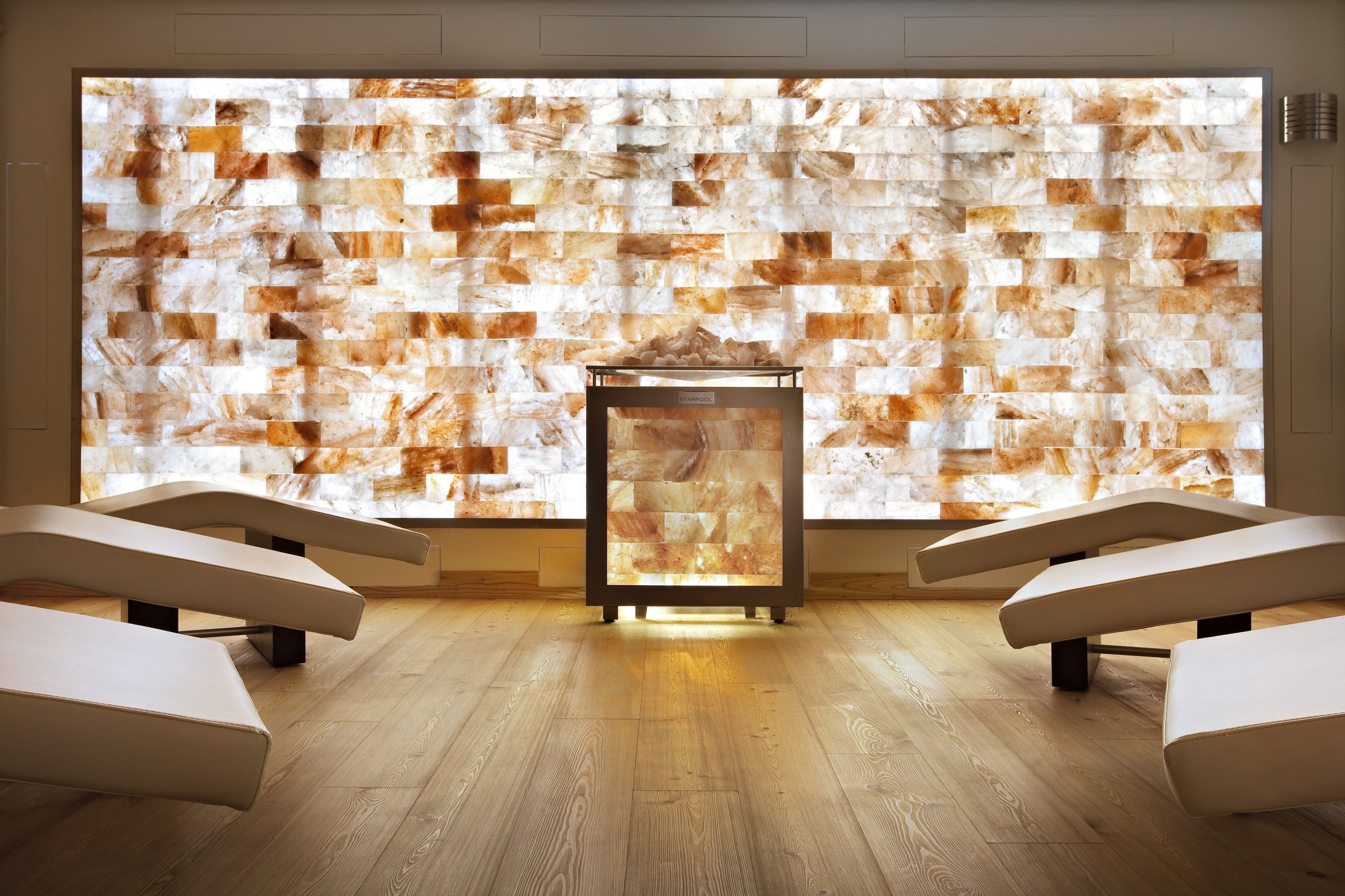 Ein Spa-Raum mit einer großen Wand aus strukturierten Paneelen, einer zentralen Glasvitrine und drei gepolsterten Sitzbereichen.
