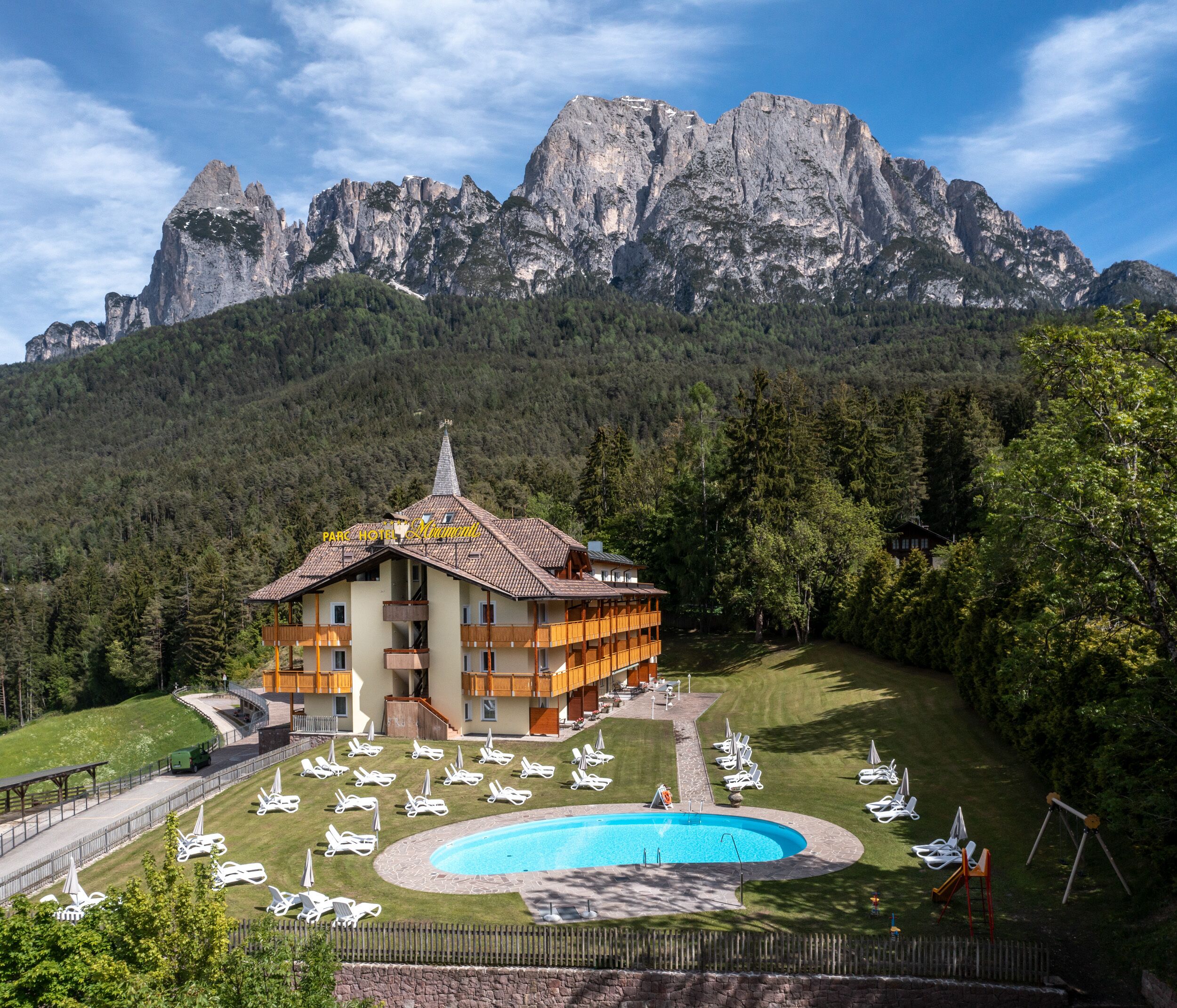 A hotel with a pool, surrounded by a forest and mountains.