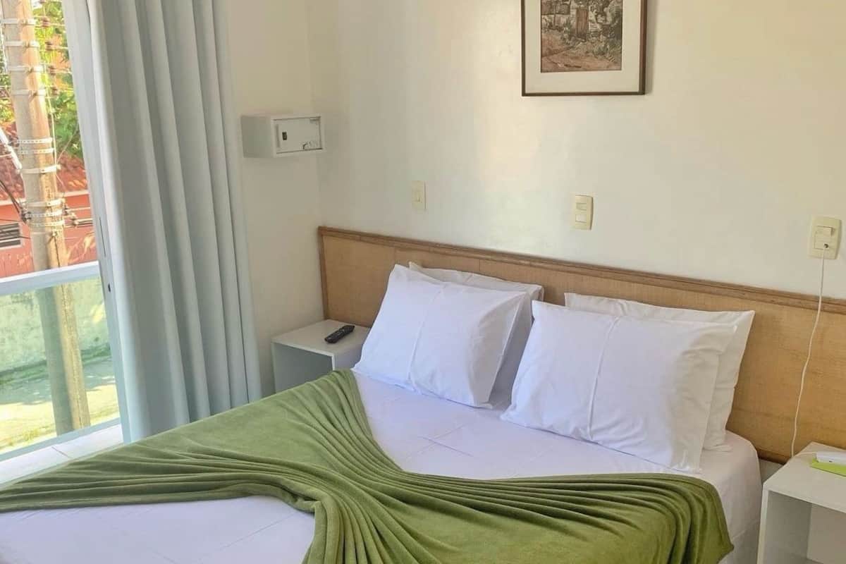 A hotel room with a bed, a nightstand, a remote control, and a window with curtains.