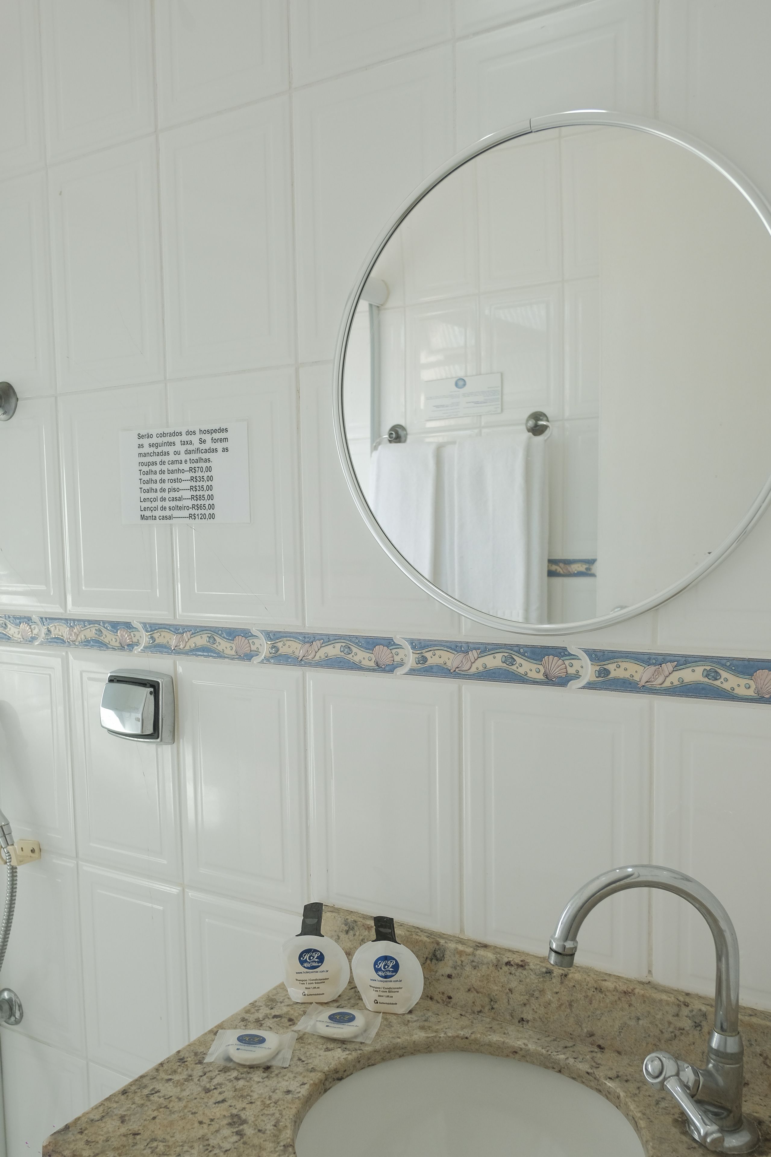 A bathroom with a sink, mirror, and toiletries. A sign lists prices for various services.