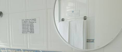 A bathroom with a sink, mirror, and toiletries. A sign lists prices for various services.