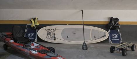 Un kayak, una pala y un vehículo eléctrico pequeño en un aparcamiento con una pared que tiene una franja amarilla.