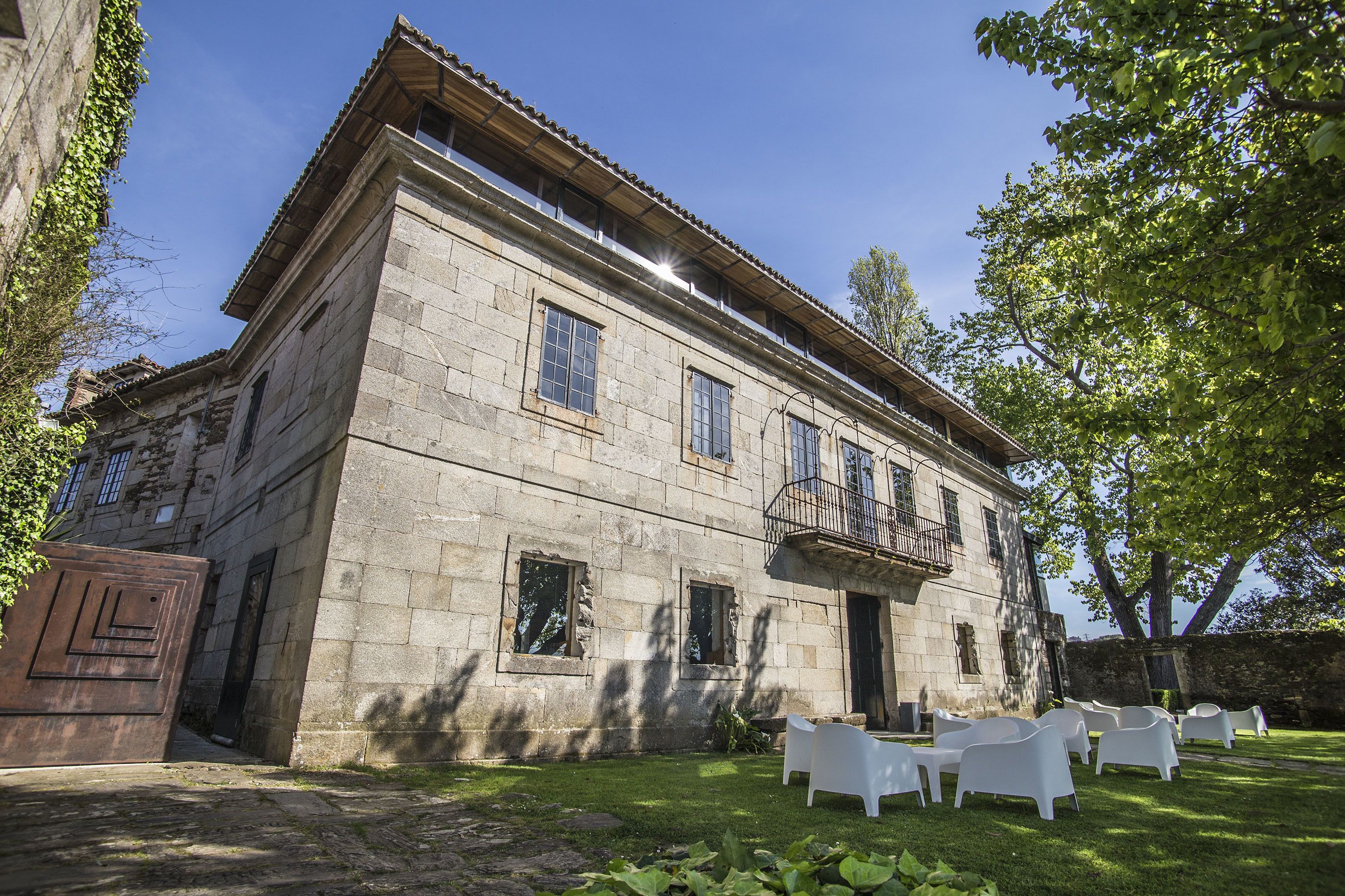 A stone building with a balcony and a lawn with white chairs.