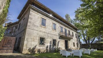 A stone building with a balcony and a lawn with white chairs.
