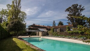 A swimming pool surrounded by a well-maintained lawn and a large house with a tiled roof. - Pazo da Merced (Neda)