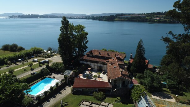 An aerial view of a property with a swimming pool, a large building with a red roof, and a lake in the background. - Pazo da Merced (Neda)