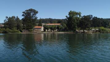 A lakeside view with a stone building with a red roof, surrounded by trees and a clear sky.