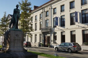 Una estatua de una mujer con corona frente a un hotel de arquitectura clásica, con balcones y un letrero que dice "HOTEL".
