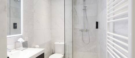 Un baño moderno con cabina de ducha de vidrio, inodoro blanco y tocador oscuro con cajones.