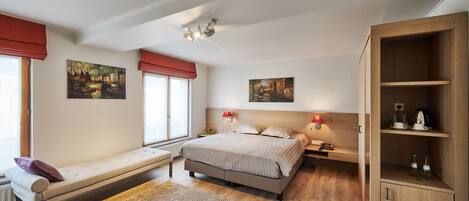 A bedroom with a bed, bedside tables, a bench, a wooden cabinet, and artwork on the walls.