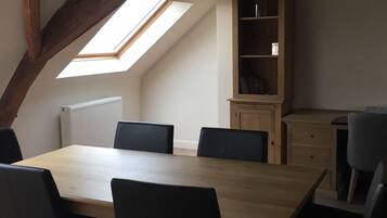 Een eetgedeelte met een houten tafel en zwarte stoelen, een inbouwboekenplank en een schuin dak met zichtbare balken.