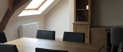 A dining area with a wooden table and black chairs, a built-in bookshelf, and a sloped ceiling with exposed beams.