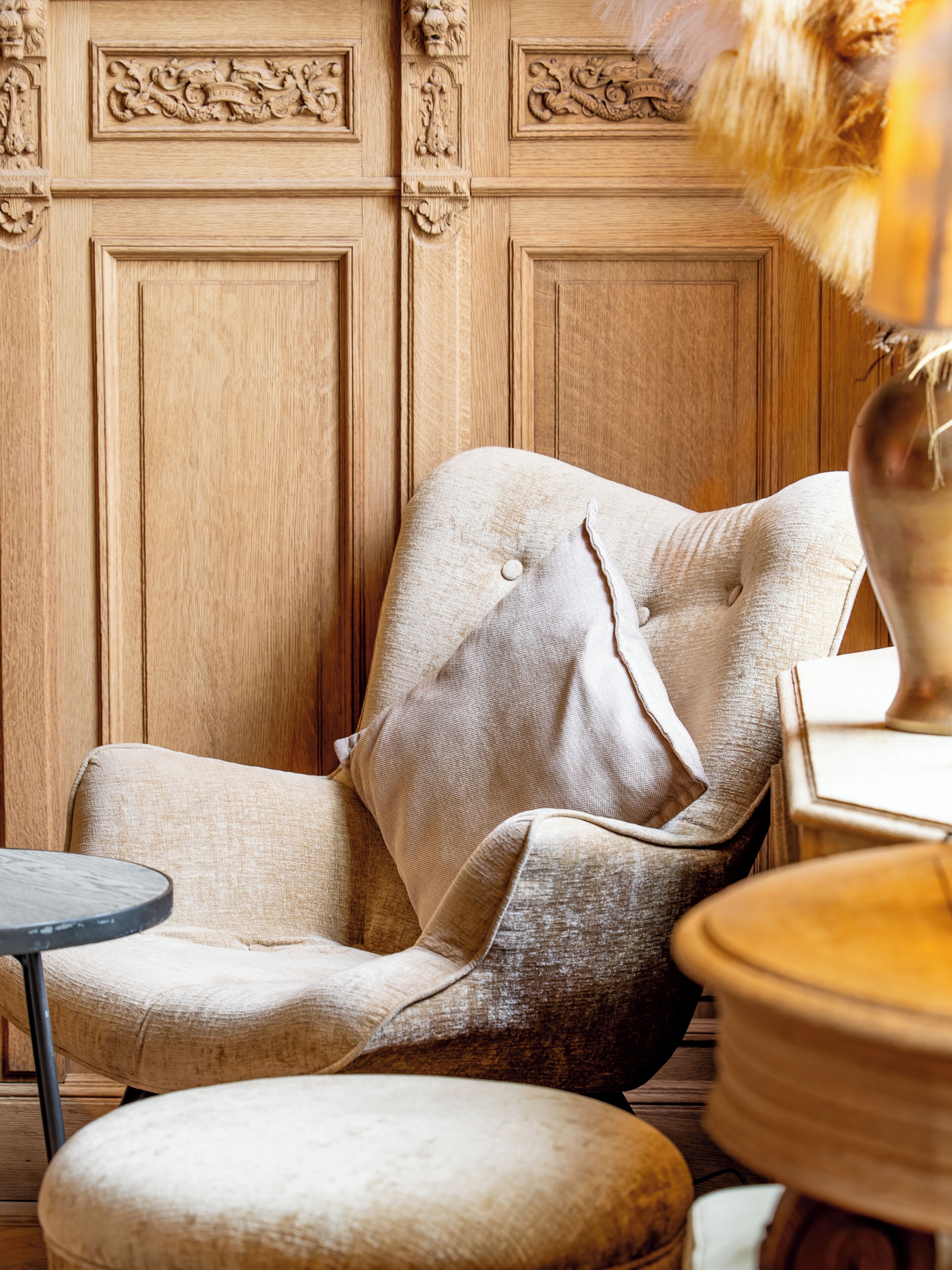 A room with a wooden paneled wall, a tufted armchair, a small round table, and a decorative vase.