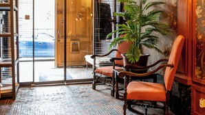 A lobby with a brick floor, wooden chairs, a potted plant, and a door leading outside. - Hotel Royal Astrid Aalst (Aalst)