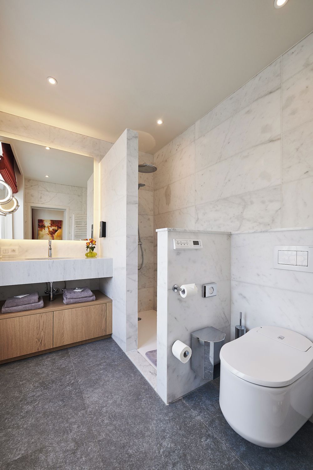 Une salle de bain moderne avec une douche en marbre, des toilettes et un meuble-lavabo avec un miroir.