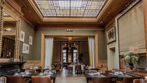 A dining area with tables set for service, a chandelier, and a large window with a view. - Hotel Royal Astrid Aalst (Aalst)