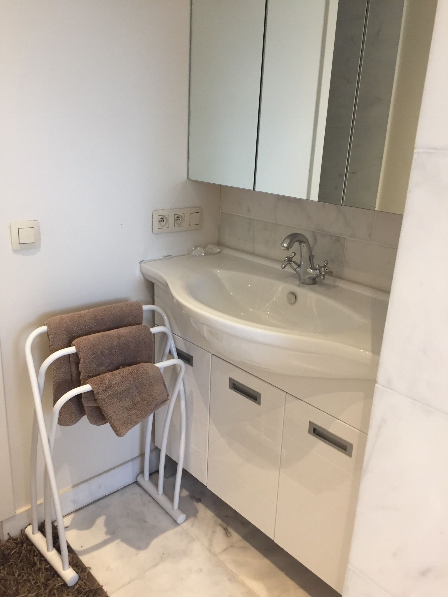 Une salle de bain avec un lavabo blanc, un miroir et un porte-serviettes avec des serviettes.