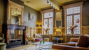 A room with a fireplace, a sofa, a coffee table, and a large window with stained glass. - Hotel Royal Astrid Aalst (Aalst)