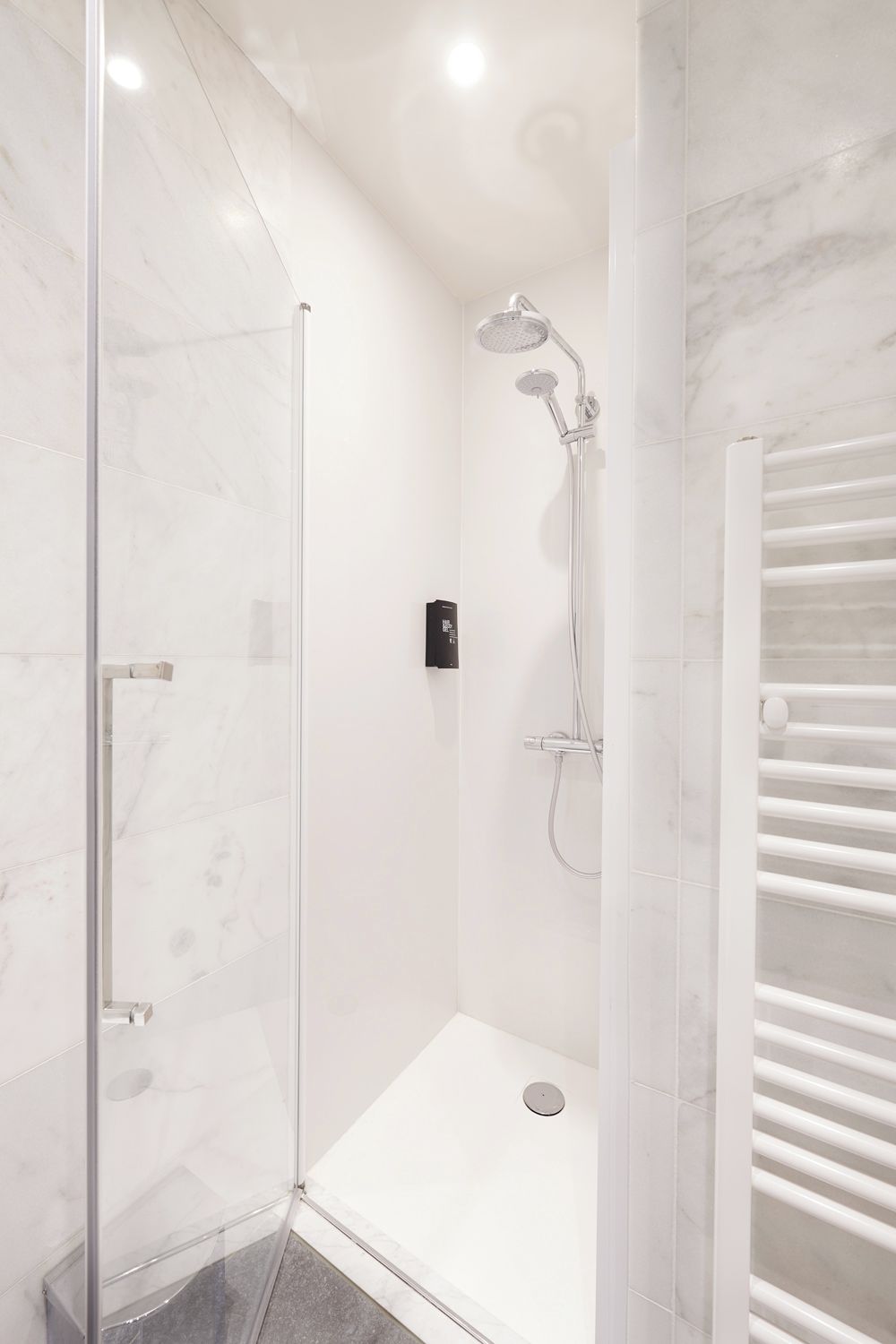 A modern bathroom with a glass shower enclosure, a built-in towel rack, and a marble-tiled shower area.