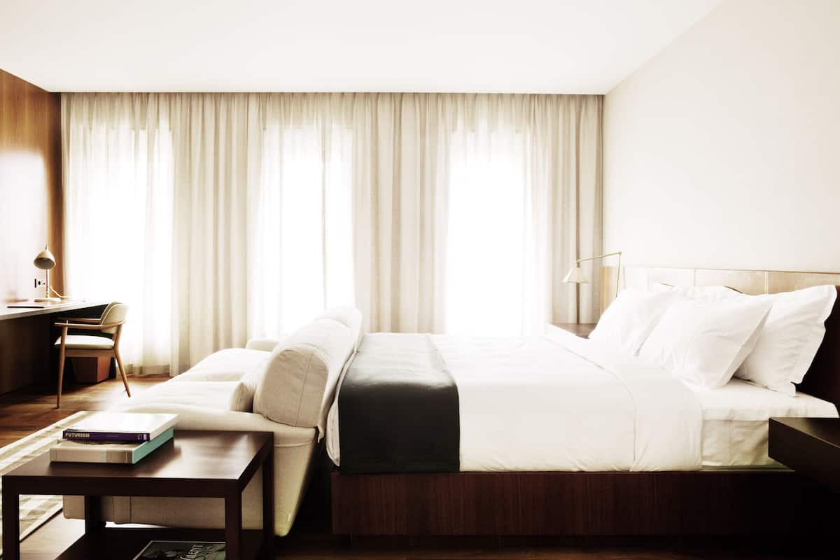 A modern hotel room with a large bed, a desk, and a chair.
