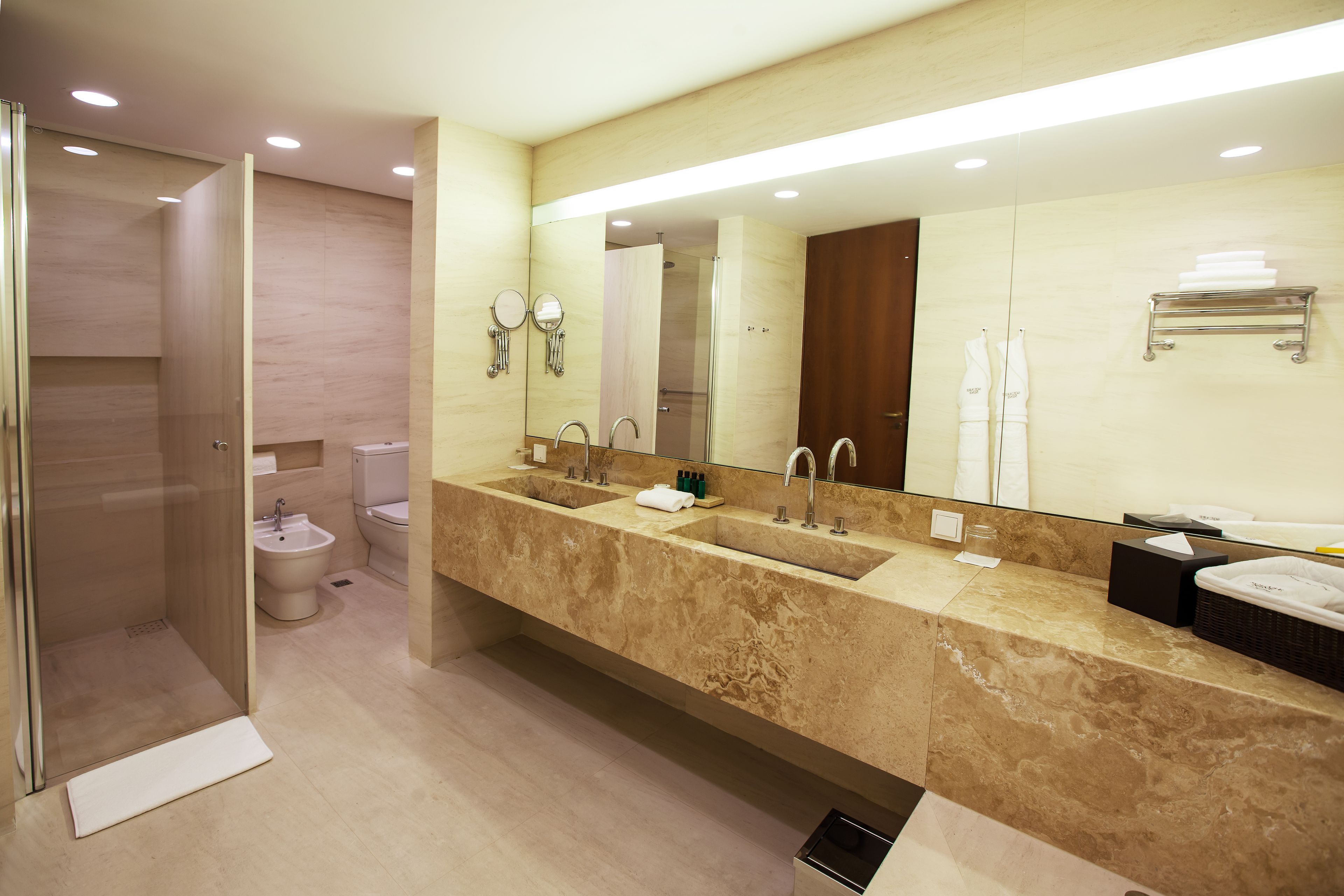 Un baño moderno con un espejo grande, dos lavamanos, una ducha y un inodoro.