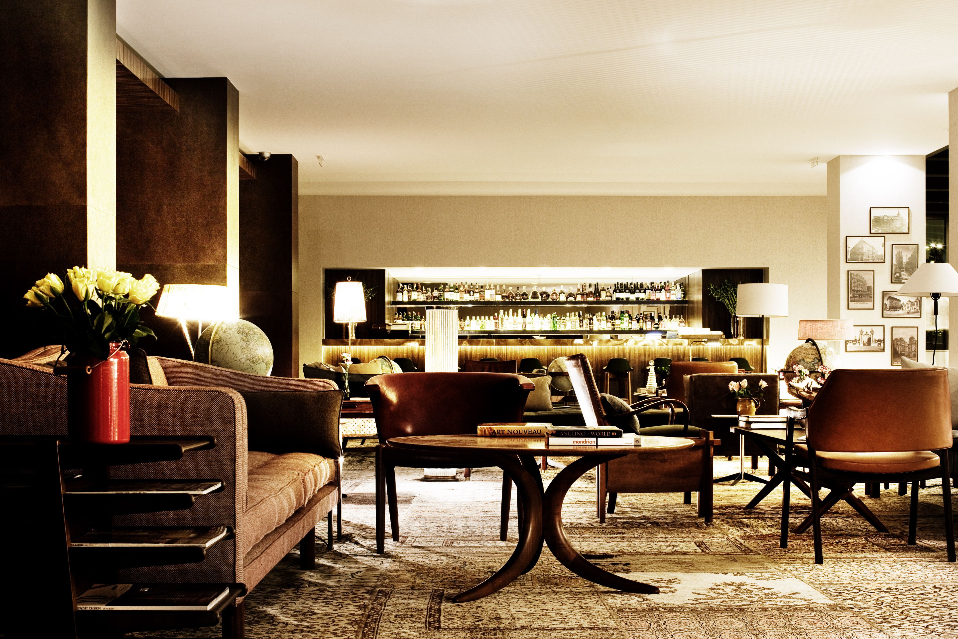 A well-lit lounge area with seating, a bar in the background, and a decorative vase with flowers.
