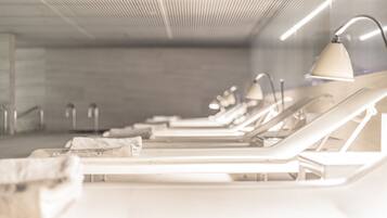 Une rangée de transats blancs équipés de lampes, un plafond en béton et une rambarde en métal.