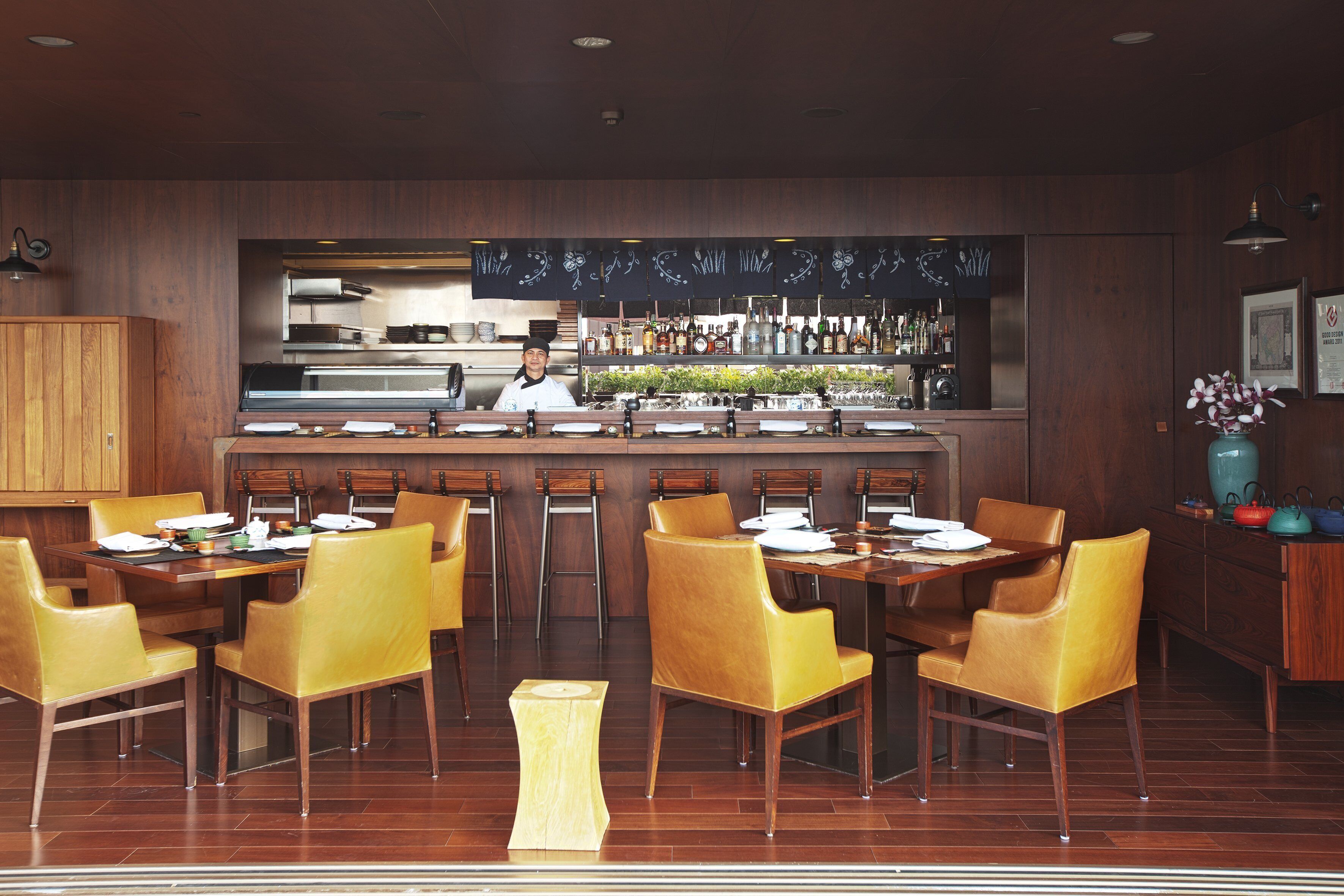 A restaurant with wooden furniture, a bar area, and a chef at the counter.