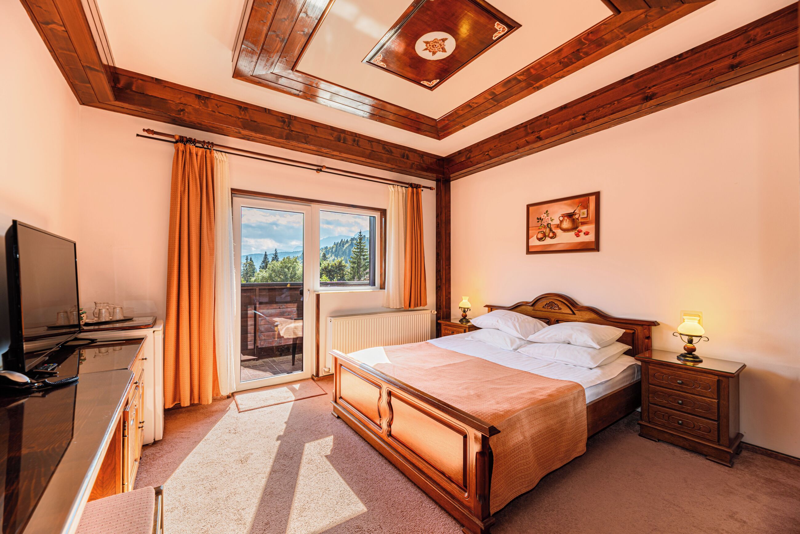 A bedroom with a bed, a dresser, a nightstand, a lamp, a window with curtains, and a ceiling with wooden beams.