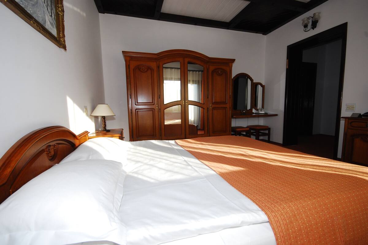 A neatly made bed with white linens, a wooden wardrobe, and a mirror above it.