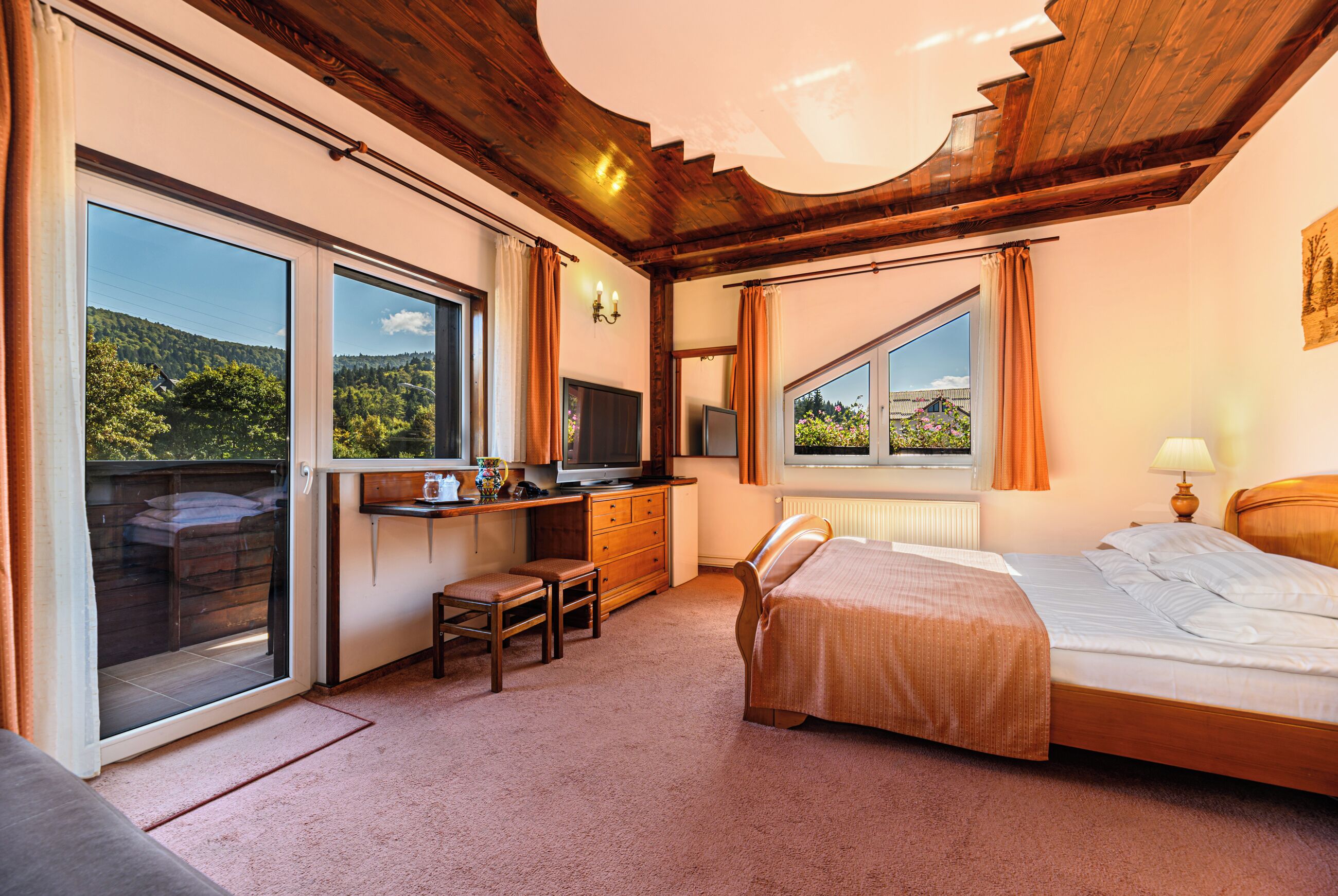 A bedroom with a bed, a desk, a chair, a television, and large windows.