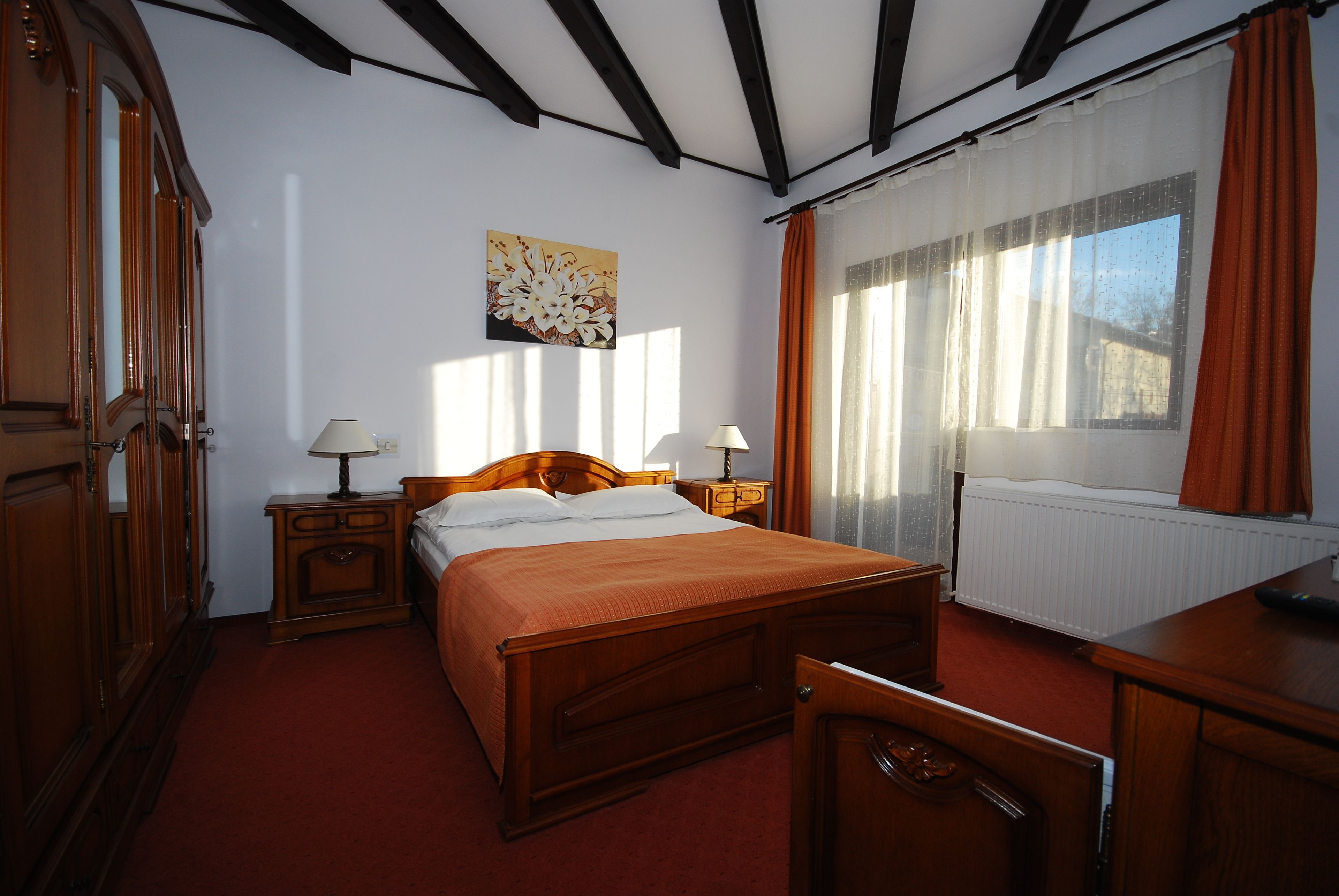 Una camera da letto con un letto in legno, due comodini con lampade, un termosifone e una finestra con tende.