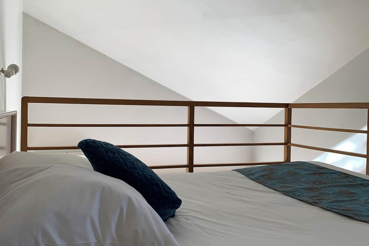 Un dormitorio con techo inclinado, cabecera de madera, cama con ropa de cama blanca y manta color turquesa.