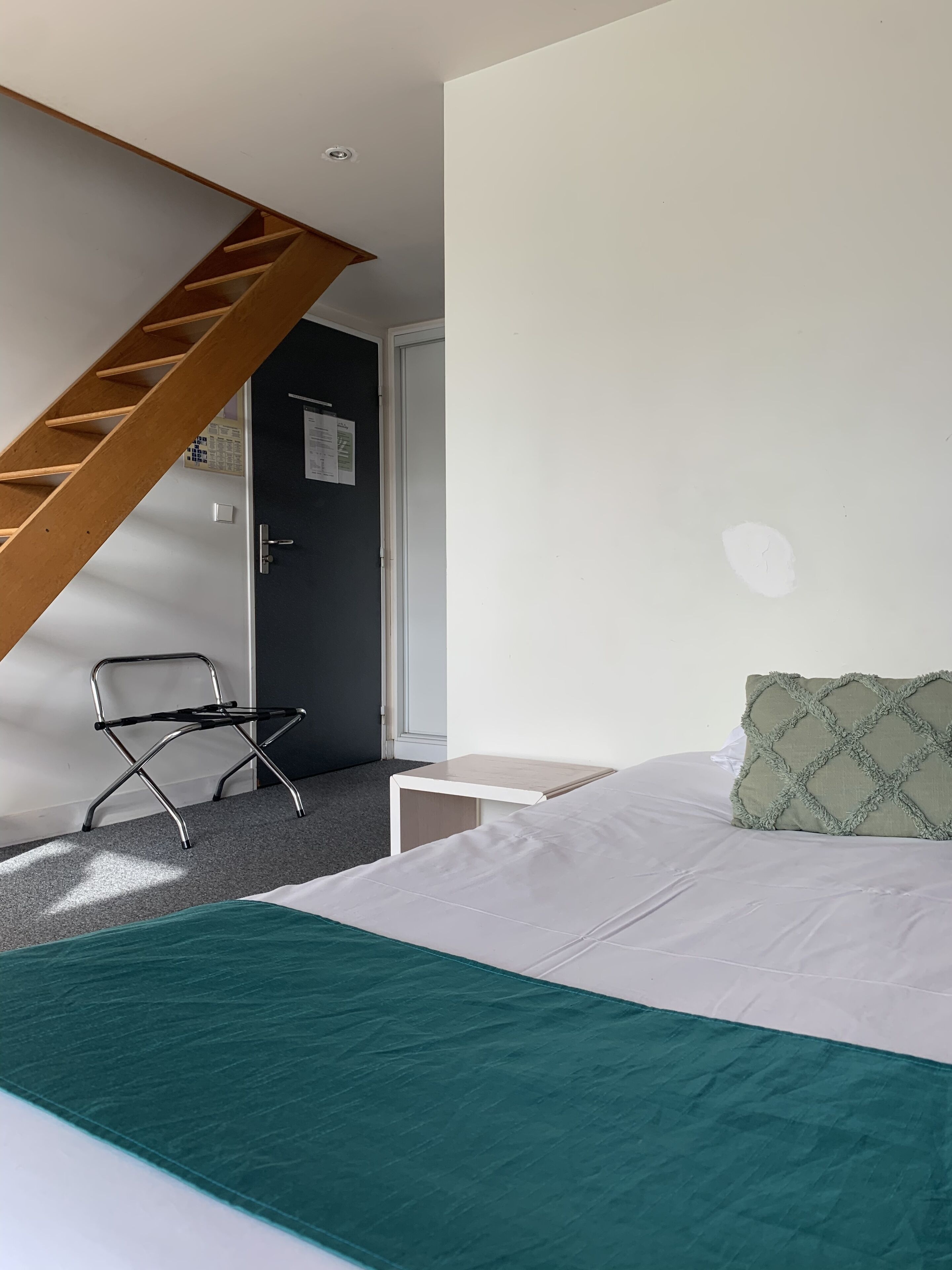 A bedroom with a bed, a chair, a nightstand, a wooden staircase, and a door.